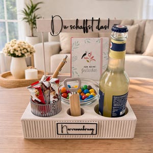 Könnte beinhalten: Ein beiges Serviertablett mit Snacks, einer Limonadenflasche und einem Notizbuch. Das Tablett enthält einen Flaschenöffner, einen Stift und eine kleine Schüssel mit bunten Süßigkeiten. Der Text "Du schaffst das!" ist oben angezeigt.