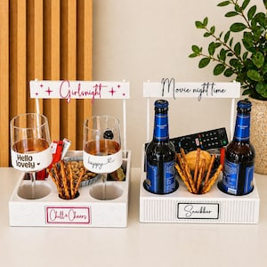 Könnte beinhalten: Zwei weiße Holzständer mit Griffen. Der linke Ständer trägt die Aufschriften "Girlsnight" und "Chill & Cheers" mit zwei Weingläsern, die mit "Hello lovely" und "happy" beschriftet sind. Der rechte Ständer zeigt "Movie night time" und "Snackbar".