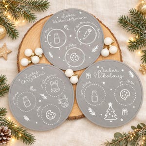 May include: Three circular grey wooden boards with white engraved holiday graphics and text. The boards feature designated spots for milk, cookies, and carrots, labelled with German text including Lieber Weihnachtsmann, Liebes Christkind, and Lieber Nikolaus.