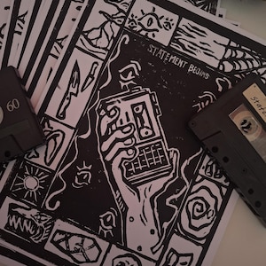 May include: A collection of black and white art prints featuring linocut illustrations. The prints depict a hand holding a device, knives, and a skull, with the text "STATEMENT BEGINS". Two cassette tapes are also included.