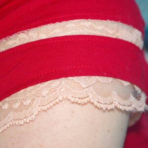 Puede incluir: Una camisa roja con un ribete de encaje blanco alrededor del cuello y las mangas. El ribete de encaje es de doble capa.