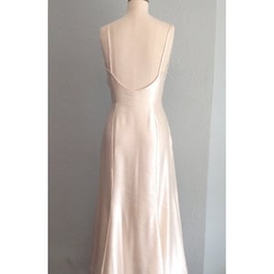 Puede incluir: Un vestido de novia sencillo, elegante, de sat&eacute;n marfil, con la espalda descubierta y una falda fluida.