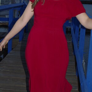 May include: A woman wearing a red off-the-shoulder dress standing on a wooden dock with a blue railing.