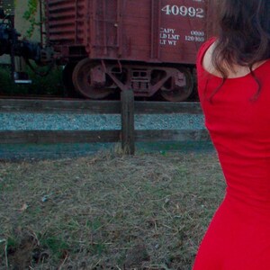 Puede incluir: Una mujer con un vestido rojo con un ribete de encaje rosa en las mangas. El vestido tiene un escote redondo y es sin mangas. La mujer est&aacute; de pie frente a un vag&oacute;n de tren rojo con el n&uacute;mero 40992 en el lateral.
