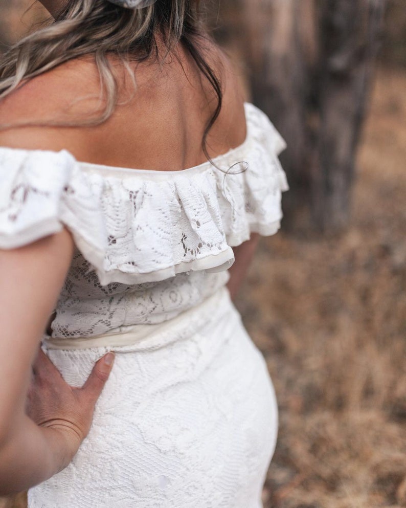 Puede incluir: Un vestido blanco de encaje de hombros descubiertos con un escote de volantes. El vestido es entallado y tiene una falda fluida.