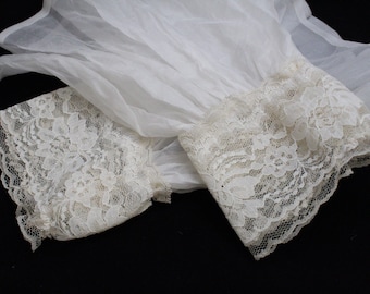 May include: White sheer fabric with delicate lace trim. The lace is a cream color and has a floral pattern.