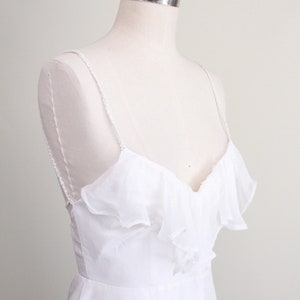 Puede incluir: Un vestido blanco sin mangas con un escote de volantes y una falda sencilla y fluida.