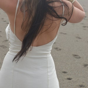 Puede incluir: Un vestido blanco sin mangas con la espalda baja y un dise&ntilde;o sencillo. El vestido est&aacute; hecho de una tela ligera y tiene una silueta fluida.