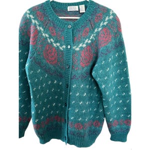 May include: A teal blue cardigan sweater with a button front and a floral pattern. The sweater has a white, pink, and purple floral design.