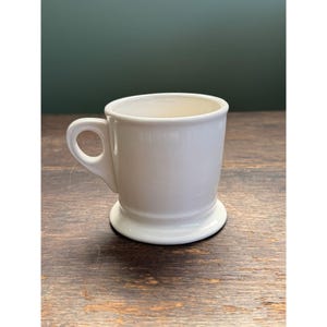 May include: A set of three ceramic mugs with a speckled, matte finish. The mugs are in shades of cream, light gray, and dark gray. Each mug has a simple, minimalist design, perfect for coffee or tea.