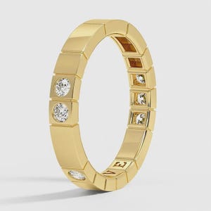 以下が含まれることがあります： 幾何学的なデザインのゴールドリング。リングは一連の長方形のセグメントを特徴とし、そのうち3つは丸く透明な宝石を含んでいます。リングはニュートラルな背景に配置され、その研磨された反射面を強調しています。