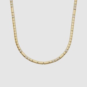 Könnte beinhalten: Eine goldene Halskette mit einem sich wiederholenden rechteckigen Kettenglied-Design. Kleine, runde, klare Edelsteine sind in die Kettenglieder eingesetzt. Die Halskette wird vor einem hellgrauen Hintergrund gezeigt.