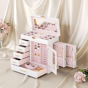 May include: A white jewelry box with multiple drawers and compartments, featuring a mirrored top and gold-colored hardware. The interior is lined with pink fabric. The box is open, revealing various jewelry pieces.