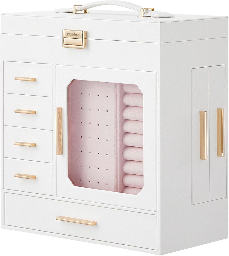 May include: A white jewelry box with multiple compartments, drawers, and a handle. The box features gold-colored hardware, including drawer pulls and a clasp. The interior is lined with pink fabric, and the box has a clear glass door.