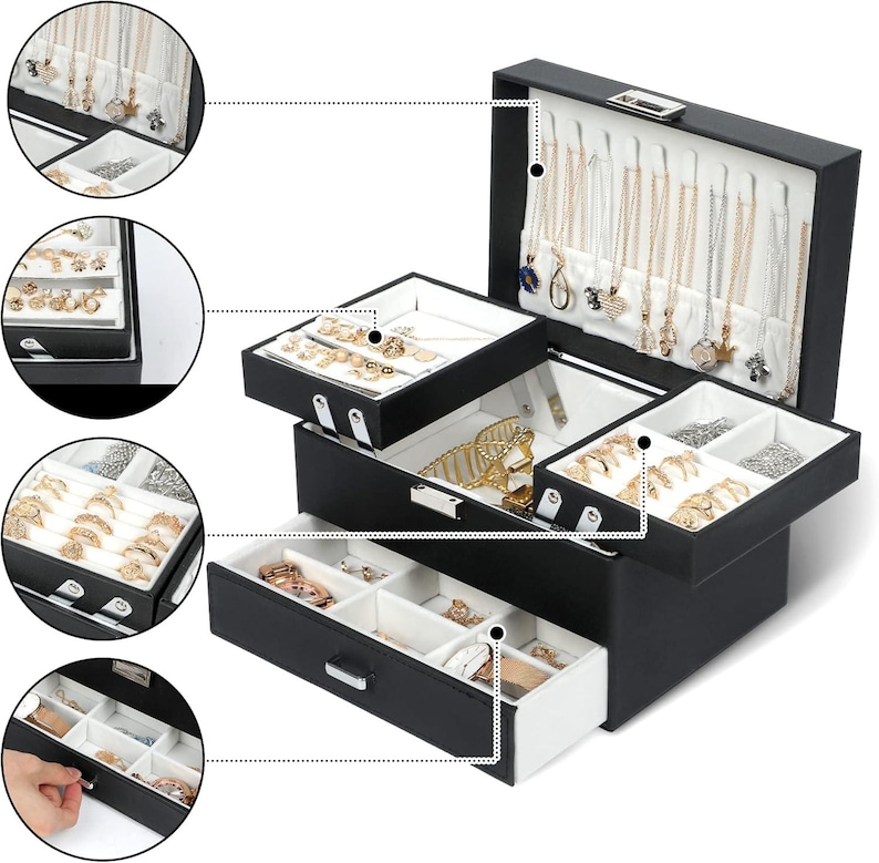 May include: A black jewellery box with a white interior, featuring a hinged lid with necklace hooks, a removable tiered tray for rings and earrings, and a bottom drawer with multiple compartments for organising various accessories and jewellery pieces.