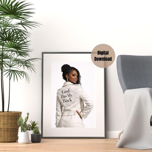 Puede incluir: Impresión digital enmarcada que muestra a una mujer con una chaqueta blanca con el texto "God Has My Back". La imagen está sobre un fondo blanco, con una silla y plantas en primer plano. Descarga digital.
