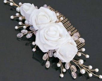 May include: White flower hair comb with pearl and crystal embellishments. The comb has a gold finish and is decorated with three white roses and pearl and crystal accents.