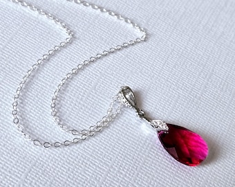 May include: A silver chain necklace with a teardrop-shaped pendant featuring a bright red crystal.