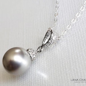May include: A silver necklace with a gray pearl pendant and a crystal-encrusted bail. The necklace is on a white background.