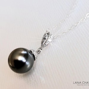 May include: A silver pendant necklace with a large, dark grey pearl. The pearl hangs from a decorative silver bail with small, sparkling accents. The delicate chain is also silver. The Lana Chayka Wedding Boutique logo is in the bottom right corner.