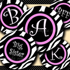 May include: Five round black and white zebra print stickers with pink circles and white text. The text on the stickers reads "B", "A", "Big Sister", "BFF", and "K".