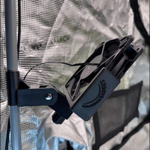 Peut inclure: Un ventilateur noir et un support de montage fixés à un poteau métallique à l'intérieur d'une tente de culture. Le ventilateur porte le texte "GROW GADGET". Le ventilateur est conçu pour faire circuler l'air.