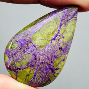 Peut inclure: Une pierre précieuse en forme de goutte d'eau, polie et présentant un motif saisissant. La base est vert olive, parcourue de veines complexes et profondes de couleur violette. La surface polie met en valeur les variations naturelles.