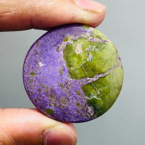Peut inclure: Une pierre précieuse ronde et polie, présentant un contraste de couleurs saisissant. La pierre est divisée en deux couleurs principales : un violet profond et un vert vif. La surface présente des veines et des motifs naturels.