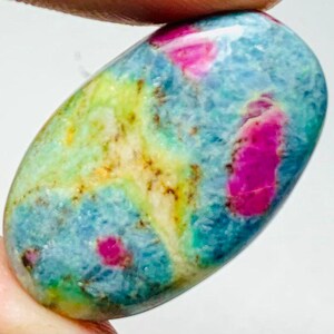 May include: An oval gemstone with a blend of colours. It has a light blue base with yellow and green patches. Bright pink spots are scattered across the stone, creating a unique pattern.