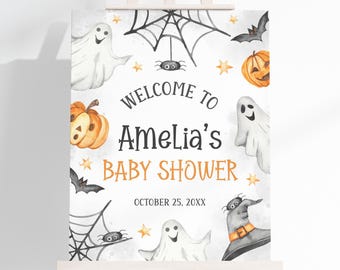 May include: A Halloween-themed baby shower sign on a wooden easel. The sign features watercolor illustrations of ghosts, pumpkins, bats, spiders, and a witch's hat. Text reads "Welcome to Amelia's Baby Shower" and "October 25, 20XX".