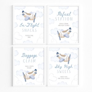 May include: Four framed prints with a watercolor airplane and cloud design. The prints have text that reads "In-Flight Snacks", "Refuel Station", "Baggage Claim", and "Sky High Sweets". The color scheme is white, blue, and tan.