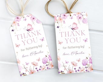 May include: Two white gift tags with floral and butterfly designs. The tags have the words "THANK YOU" in a soft purple font, along with the phrase "for fluttering by!" and the name "Amelia". Each tag has a twine string.