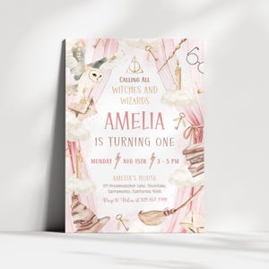 以下が含まれることがあります： 「Calling All Witches and Wizards」と「Amelia is Turning One」の文字が入ったピンクと白の招待状。フクロウ、雲、ほうき、その他の魔法の要素がデザインされています。日付は8月15日です。