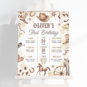 May include: A watercolor-style birthday sign on an easel. The sign has a cowboy theme with a hat, boots, and horseshoe illustrations. The text reads "Oliver's First Birthday" and includes personal details like height (20 inches) and weight (28 pounds).