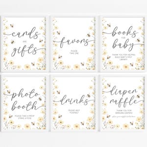 May include: Six framed signs with white backgrounds and floral and bee accents. The signs read "cards and gifts", "favors", "books for baby", "photo booth", "drinks", and "diaper raffle".