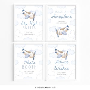 May include: Four framed signs with a baby shower theme. Each sign features a watercolor illustration of a biplane and clouds. Text on the signs includes "Sky High Sweets", "Make an Aeroplane", "Photo Booth", and "Advice and Wishes".