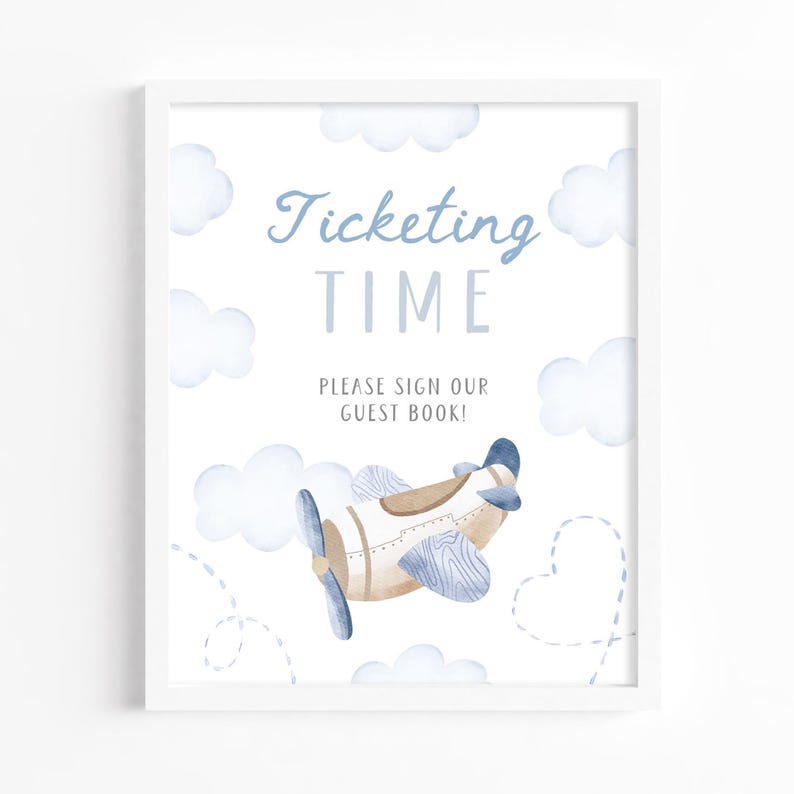 May include: A framed print with a watercolor illustration of a vintage airplane and clouds. The text reads "Ticketing Time, Please Sign Our Guest Book!" in blue and gray lettering. The artwork has a soft, pastel color palette.