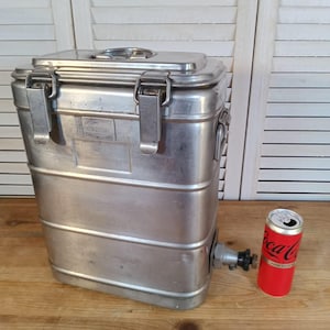 Peut inclure: Un grand récipient rectangulaire en acier inoxydable avec un couvercle à charnière et deux loquets. Il possède un robinet sur le côté et une canette de Coca-Cola à côté. Le récipient est probablement destiné au stockage d'aliments ou de boissons.
