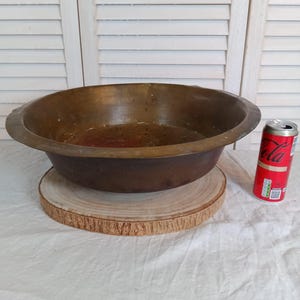 Peut inclure: Un grand bol en bronze antique avec un large bord, posé sur une tranche de bois ronde. Une canette de soda rouge et blanche est à côté du bol. Le bol mesure environ 30 cm de diamètre.