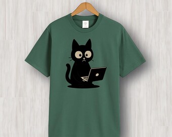 May include: Green t-shirt featuring a black cat cartoon with large eyes, sitting and using a laptop. The cat is the central focus, set against a solid green background. The shirt is hanging on a wooden hanger.
