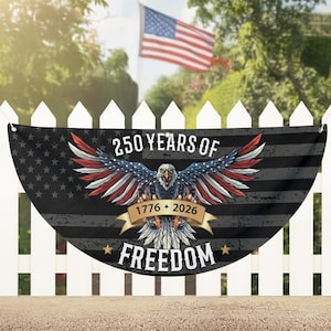 Puede incluir: Bandera con el texto "250 YEARS OF FREEDOM 1776-2026" y un diseño de águila con alas rojas, blancas y azules. La bandera cuelga de una valla blanca, con una bandera americana ondeando al fondo.