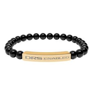 Könnte beinhalten: Ein Armband aus schwarzen Perlen mit einem goldfarbenen rechteckigen Steg. Auf dem Steg steht in Grau der Text "DRS ENABLED". Das Armband besteht aus runden, polierten schwarzen Perlen.