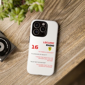 May include: White phone case with the text "LECLERC RADIO" and the number "16" in red. The case features quotes like "IS THERE A LEAKAGE?" and "I HAVE THE SEAT FULL OF WATER!" with the Ferrari logo.
