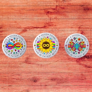 Peut inclure: Trois badges ronds blancs avec le texte "I HAVE A HIDDEN DISABILITY PLEASE BE PATIENT WITH ME". Chaque badge présente un design différent : un symbole infini, un tournesol et un papillon, tous aux couleurs vives.