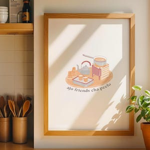 May include: A framed print featuring a tea-themed illustration with a teapot, cups, and a small stove. The artwork is in a wooden frame and is displayed on a kitchen counter. The text "ajo friends cha peelo" is visible on the print.