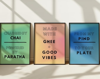May include: Three framed art prints with black frames and colorful backgrounds. The prints feature text: "CHARGED BY CHAI POWERED BY PARATHA", "MADE WITH GHEE + GOOD VIBES", and "FROM MY PIND TO YOUR PLATE".