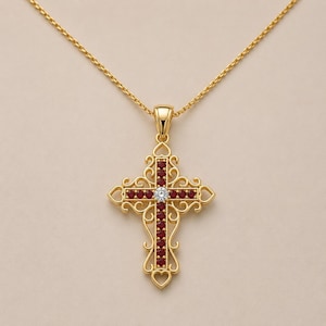 May include: A gold cross pendant necklace featuring an intricate filigree design with heart-shaped accents at the terminals. The cross is set with a vertical row of deep red gemstones and a single clear, round-cut stone at the center intersection.