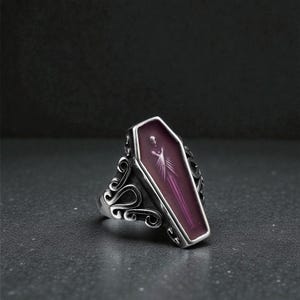K&ouml;nnte beinhalten: Ein silberner Ring mit Sarg-Design, lila Innenraum und einer Figur. Der Ring hat verzierte Schn&ouml;rkel an den Seiten, was ihm einen gotischen Look verleiht. Der Ring ist vor einem dunklen Hintergrund platziert.