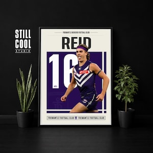 May include: A framed poster featuring a Fremantle Dockers Football Club player wearing a purple and white jersey with the number 16. The text reads REID, FREMANTLE DOCKERS FOOTBALL CLUB, and FREMANTLE FOOTBALL CLUB. The design includes a large purple square.
