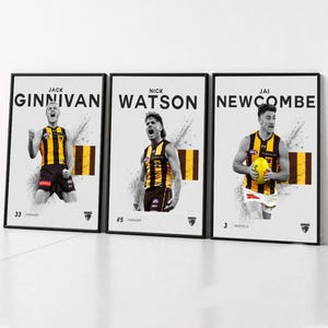 Puede incluir: Tres pósteres enmarcados con los jugadores de fútbol australiano Jack Ginnivan, Nick Watson y Jai Newcombe. Cada impresión muestra al atleta con una camiseta marrón y dorada, su nombre en negrita, su número de jugador y los logotipos del equipo.